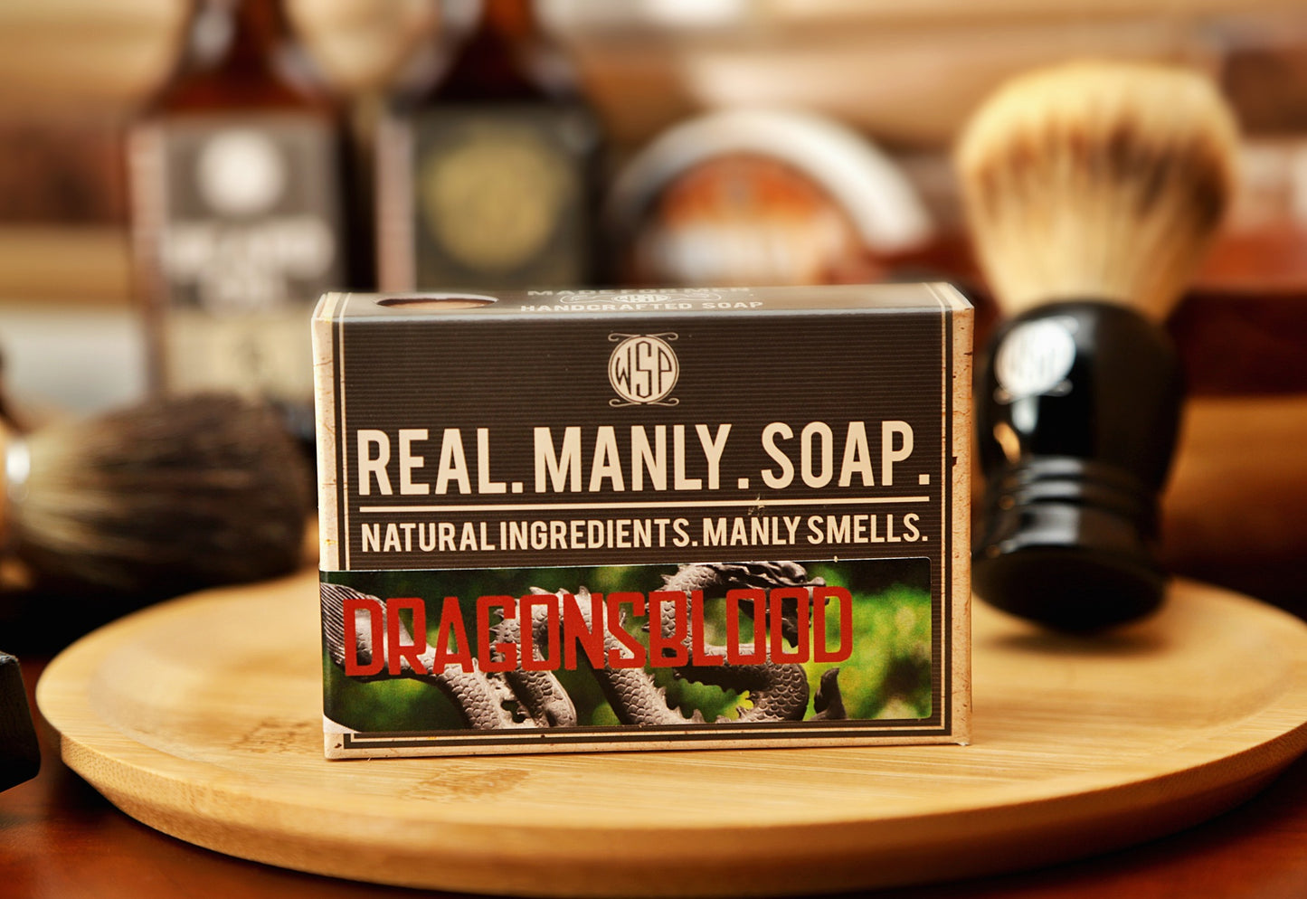 Bar of soap with 'Real Manly Soap' Dragonsblood scent packaging on a wooden tray, surrounded by shaving tools.