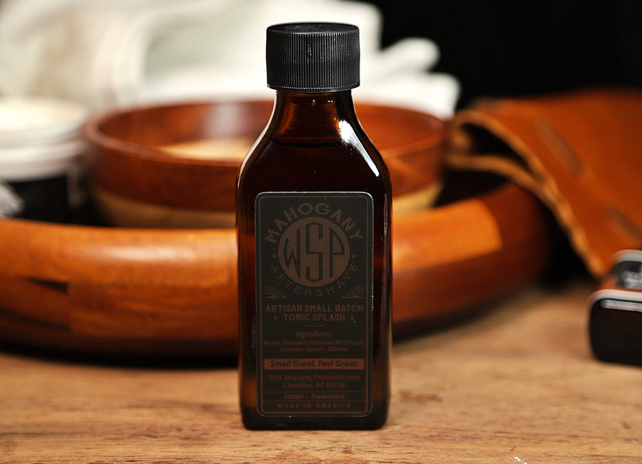 Small brown bottle of WSP Mahogany Aftershave Tonic splash sitting on table with white towel