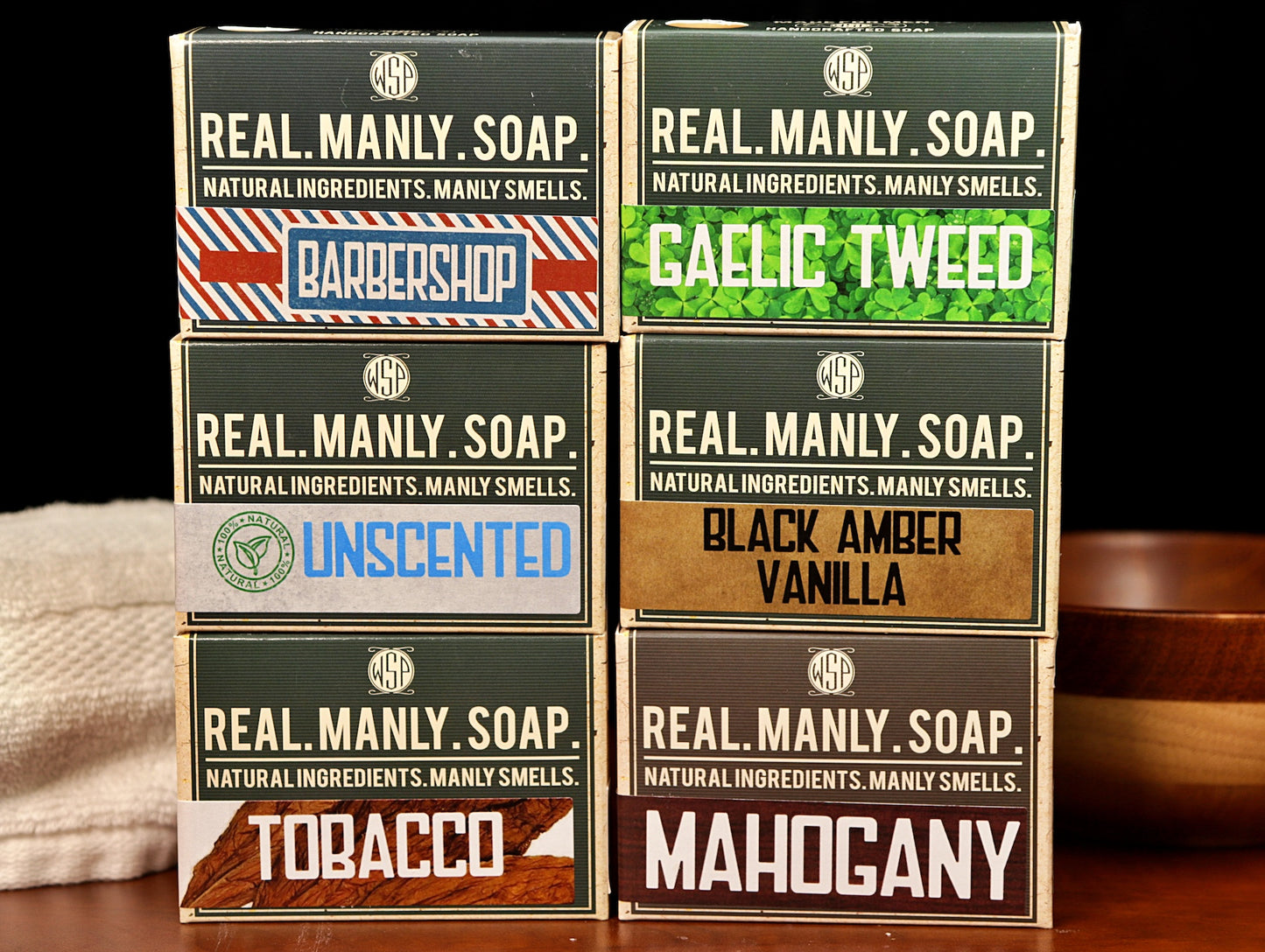 A set of 6 boxes of WSP bar soaps sitting on a table with a towel and bowl in the background.