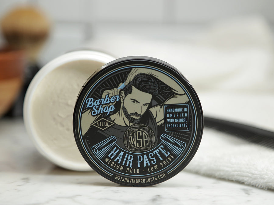Tub on its side showing the Barbershop-scented hair paste inside with the lid placed nearby