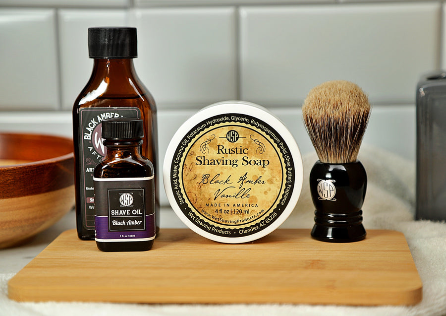 WSP Shaving Set of Black Amber Vanilla shave oil, rustic shaving soap, aftershave tonic and shaving brush all sitting on wooden board with white towel