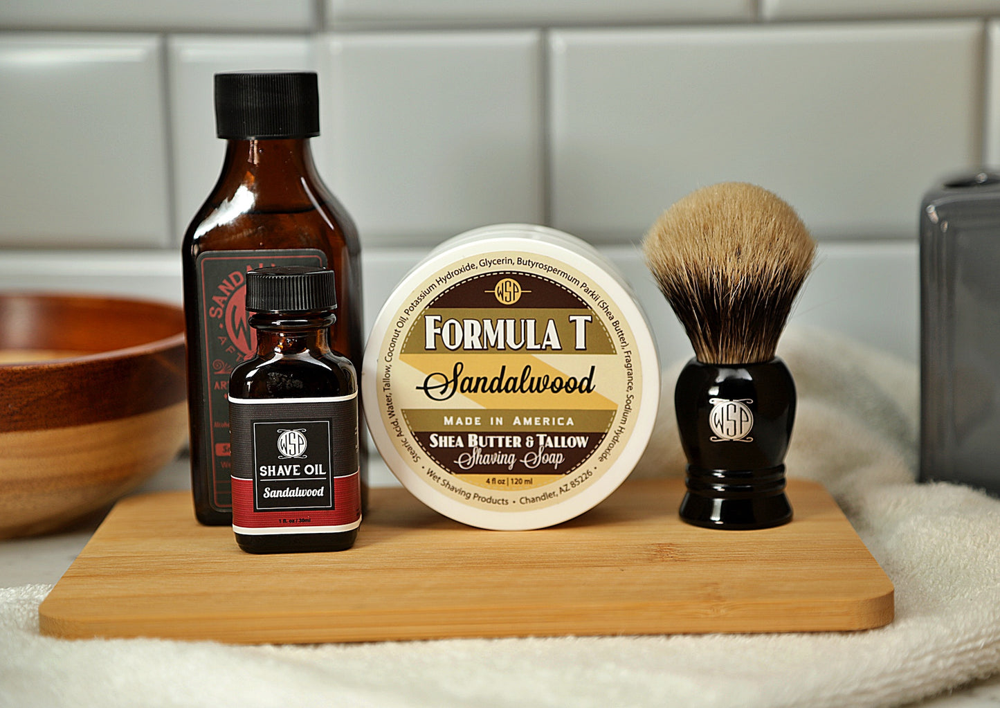 WSP Shaving Set of Sandalwood shave oil, rustic shaving soap, aftershave tonic and shaving brush all sitting on wooden board with white towel