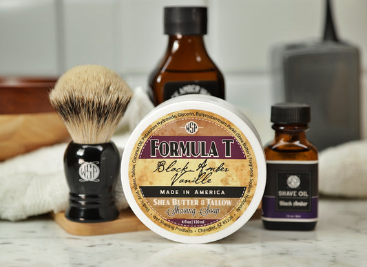 Shaving Set of Black Amber Vanilla shave oil, rustic shaving soap, aftershave tonic and shaving brush all sitting on wooden board with white towel