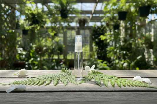 Clear spray bottle on a wooden table with green leaves and white flowers in a garden setting
