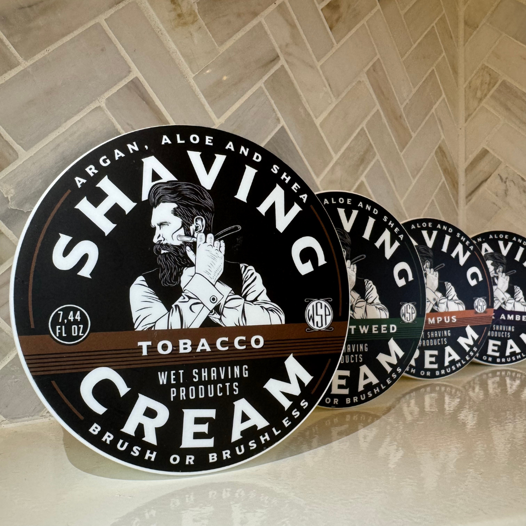 Travel size shaving cream containers in a row with 'SHAVING CREAM' text visible on the labels, indicating a tobacco scent.