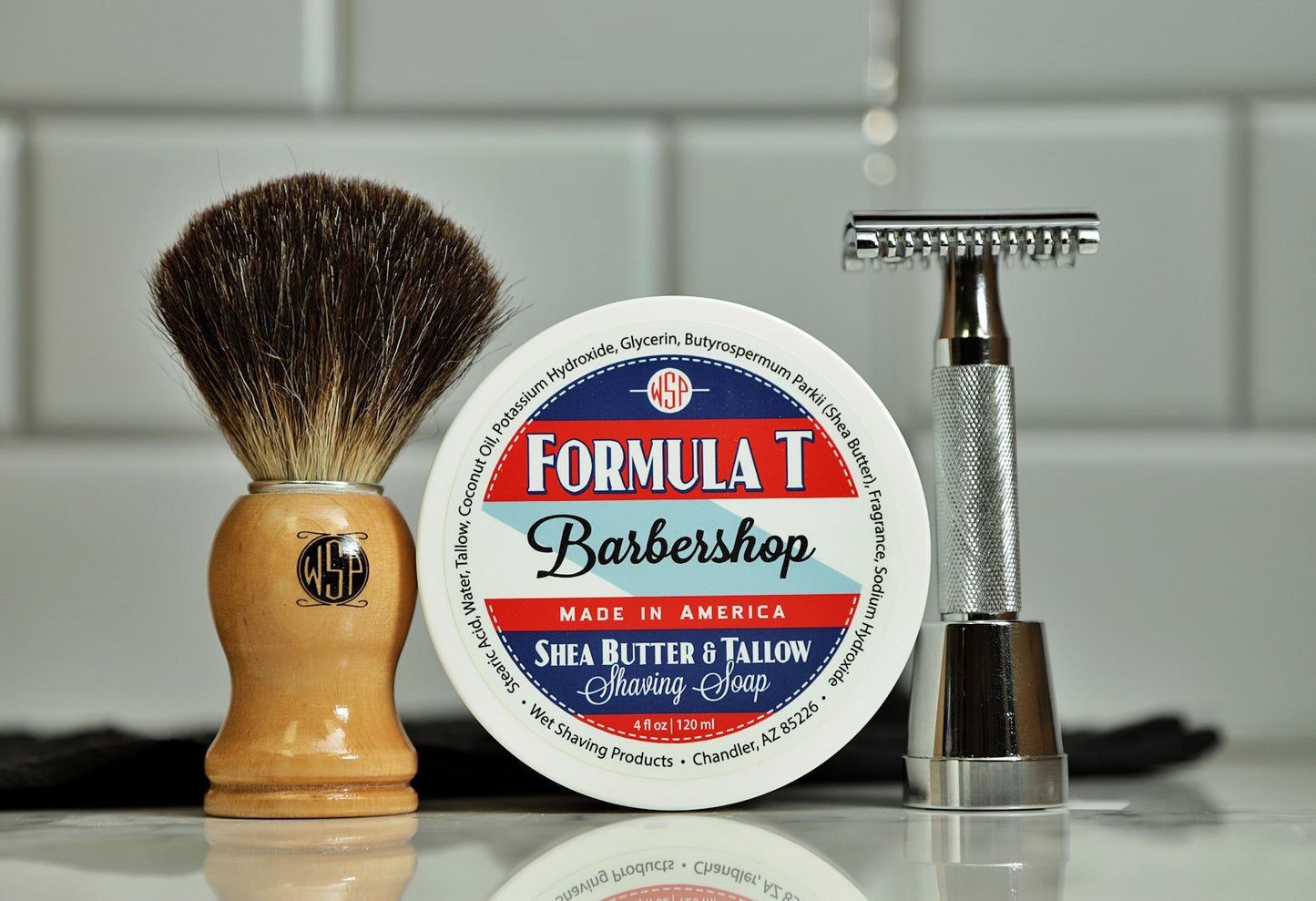 The image shows a shaving kit consisting of a black badger brush with a wooden handle, a round container of shaving soap labeled 'Formula T Barbershop', and a safety razor.