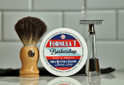 The image shows a shaving kit consisting of a black badger brush with a wooden handle, a round container of shaving soap labeled 'Formula T Barbershop', and a safety razor.