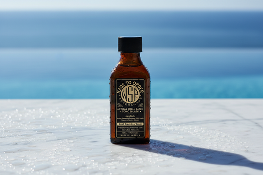 WSP aftershave splash Centered on a cool white Carrara marble slab covered in fresh water droplets and cold condensation, bright cool morning daylight striking the surface, out of focus background suggesting a clean blue pool edge or ocean horizon, refreshing atmosphere, sharp focus, photorealistic render, 8k resolution.
