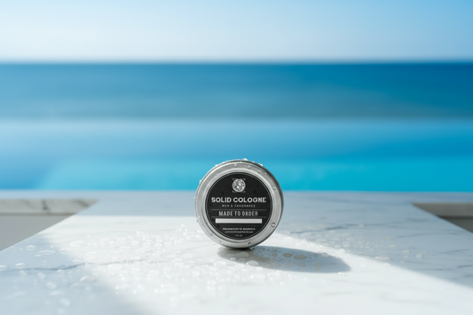 WSP solid cologne centered on a cool white Carrara marble slab covered in fresh water droplets and condensation, bright cool morning daylight striking the surface, out of focus background suggesting a clean blue pool edge or ocean horizon, refreshing atmosphere, sharp focus, photorealistic render, 8k resolution.