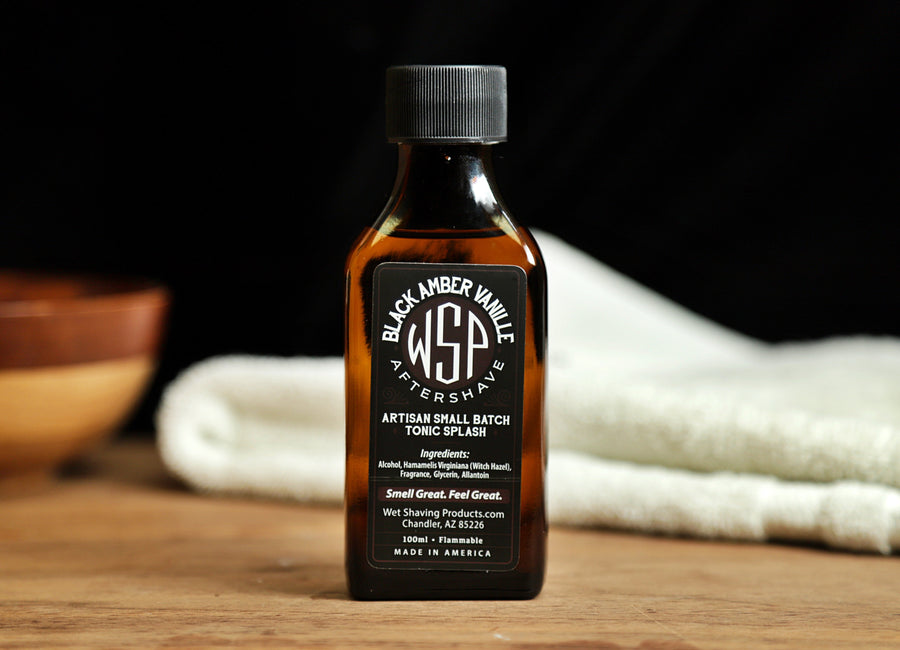 Small brown bottle of WSP Black Amber Vanilla Aftershave Tonic splash sitting on table with white towel