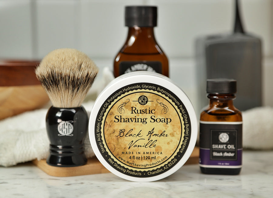 WSP Shaving Set of Black Amber Vanilla shave oil, rustic shaving soap, aftershave tonic and shaving brush all sitting on wooden board with white towel