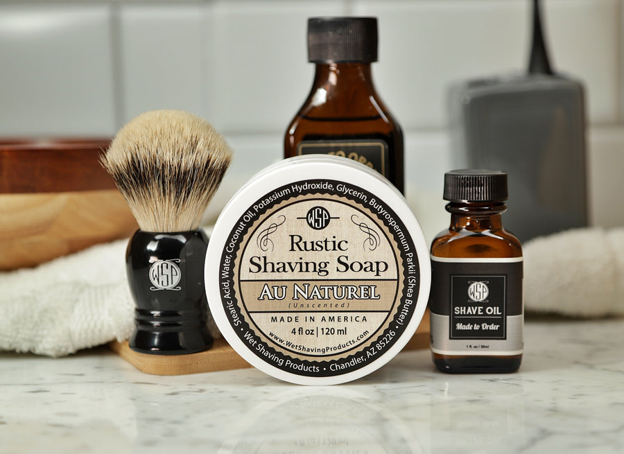 WSP Shaving Set of Au Natural shave oil, rustic shaving soap, aftershave tonic and shaving brush all sitting on wooden board with white towel