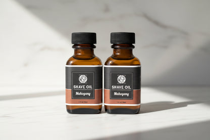 Two bottles of shave oil with black labels on a countertop.