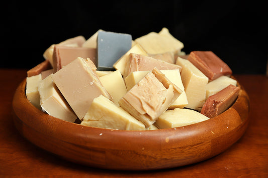 A variety of soap bars in different colors and shapes displayed in a wooden bowl.