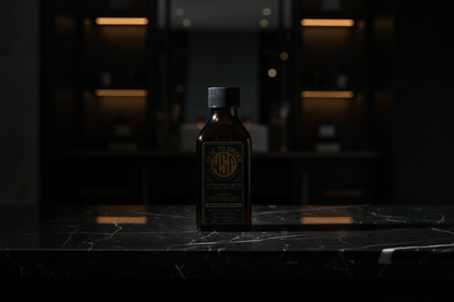 wsp aftershave splash Sitting on a polished black marble surface with faint white veining, dramatic side lighting creating a chiaroscuro effect, dark blurred background suggesting a high-end master bathroom or dressing room with hints of warm amber light, sleek, minimalist luxury, photorealistic, 8k resolution, deep depth of field.
