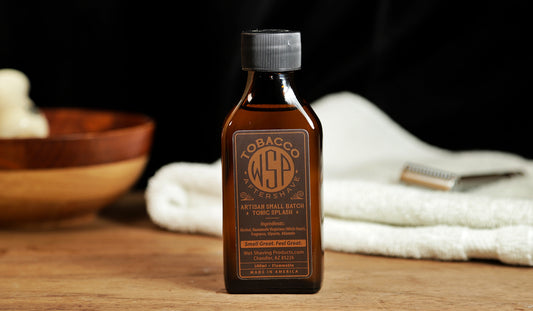 Small brown bottle of WSP Tobacco Aftershave Tonic splash sitting on table with white towel