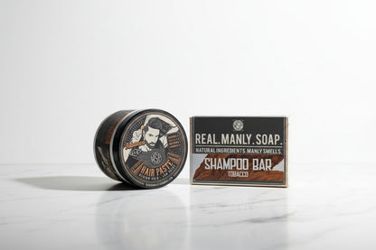 Hair paste container and shampoo bar packaging on a countertop with a tiled backsplash.