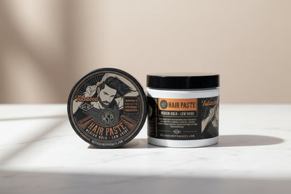 Two Hair paste jars sitting on a clean, polished white Carrara marble surface with faint grey veining, bright clean morning light from the left, out of focus pale neutral background, premium spa atmosphere, sharp focus on the product.