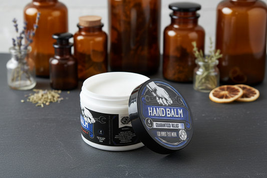 WSP Hand Balm Centered on a dark honed slate surface, soft natural daylight streaming from the side, out of focus background featuring vintage amber glass apothecary jars and dried botanical herbs in small glass containers, clean, natural, artisanal atmosphere, macro photography style, shallow depth of field, sharp focus on the product, photorealistic render.