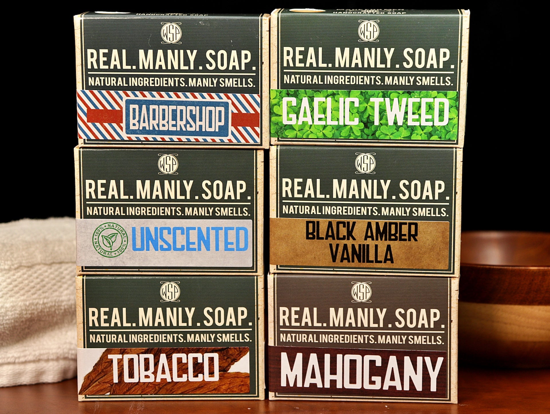 A set of 6 boxes of WSP bar soaps  sitting on a table with a towel and bowl in the background.