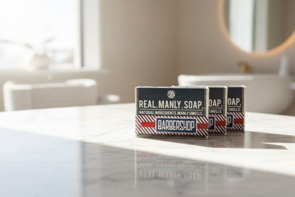 Two boxes of Real Manly Soap on a wooden surface with a blurred background.