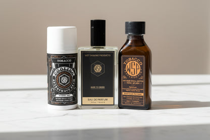 Three bottles of men's grooming products sitting on a clean, polished white Carrara marble surface with faint grey veining, bright clean morning light from the left, out of focus pale neutral background, premium spa atmosphere, sharp focus on the product.
