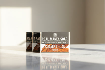 Three boxes of Real Manly Soap on a reflective surface with a neutral background