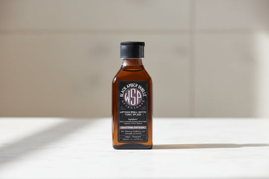 Bottle of Black Amber aftershave splash on a white surface with a neutral background